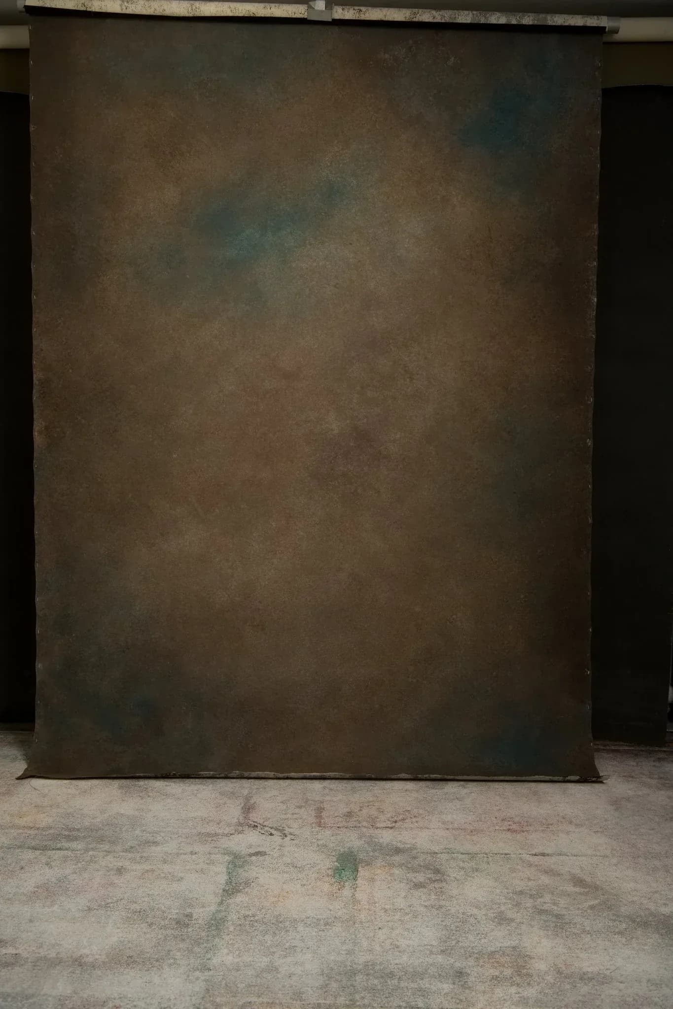 Warm brown hand-painted canvas backdrop hanging on a roller in a working studio with a painted floor