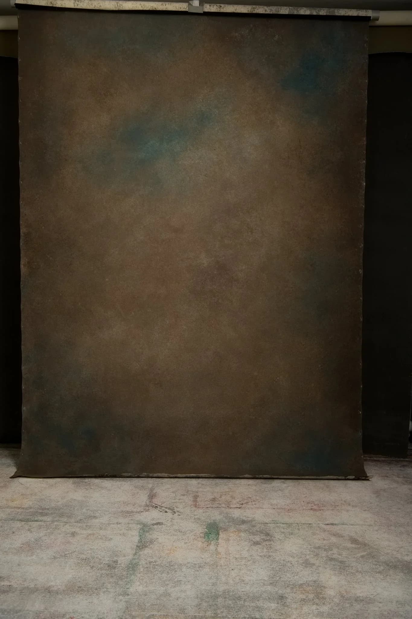 A warm brown hand-painted canvas backdrop with soft blue and rose patches, hung floor to ceiling in the studio