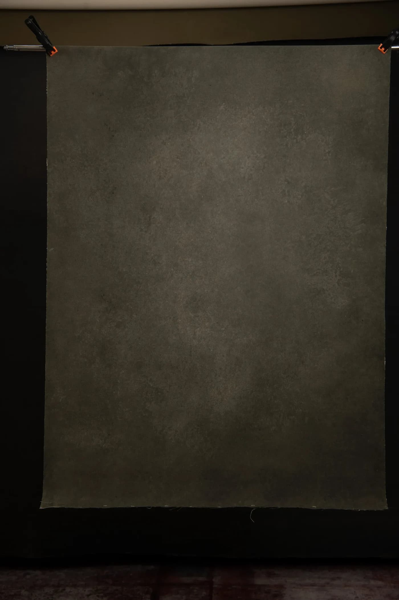 Dark charcoal hand-painted canvas backdrop clamped to a crossbar, tonal variation visible across the surface
