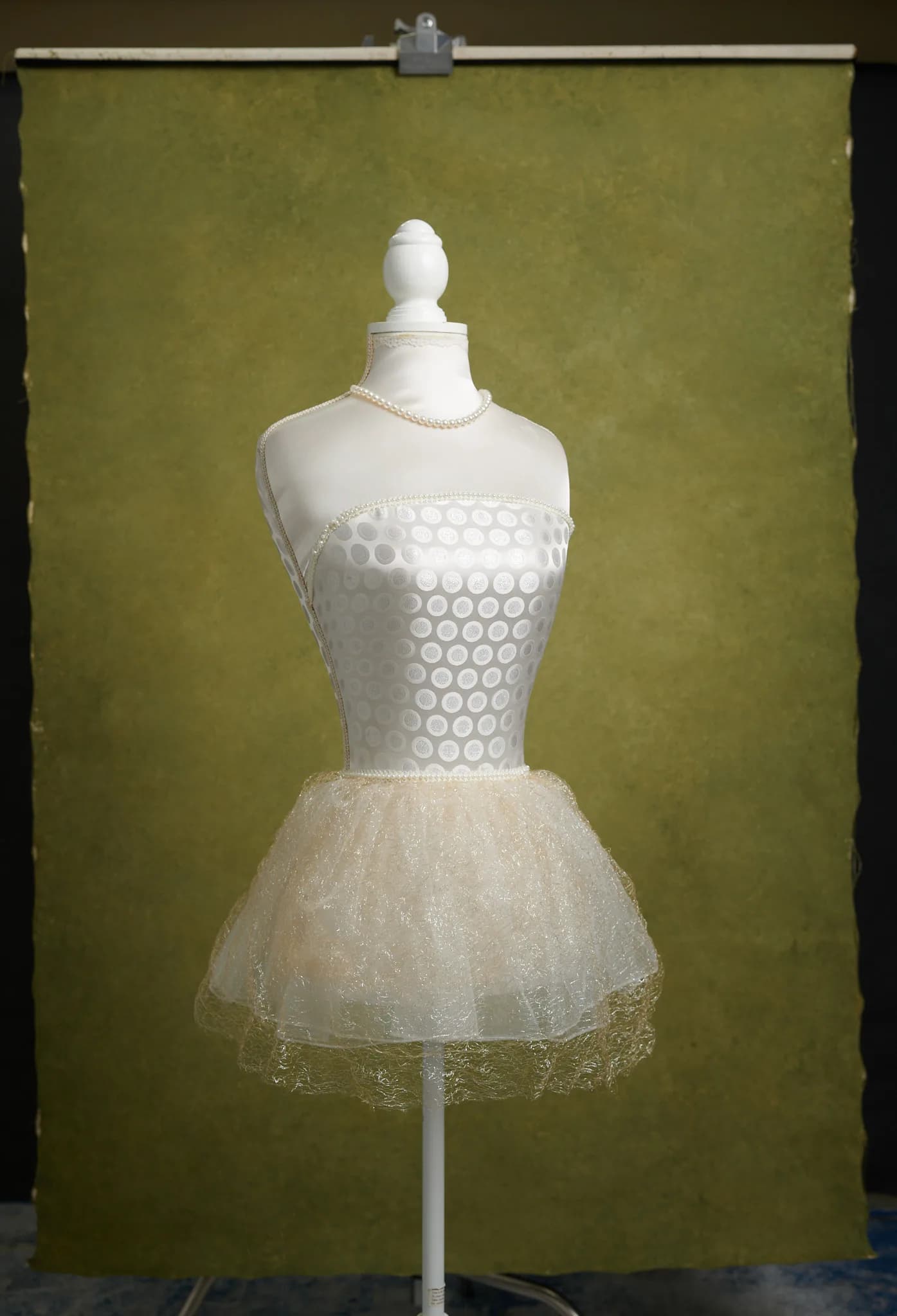 An olive green hand painted canvas backdrop hanging full length with a white dress form standing in front of it