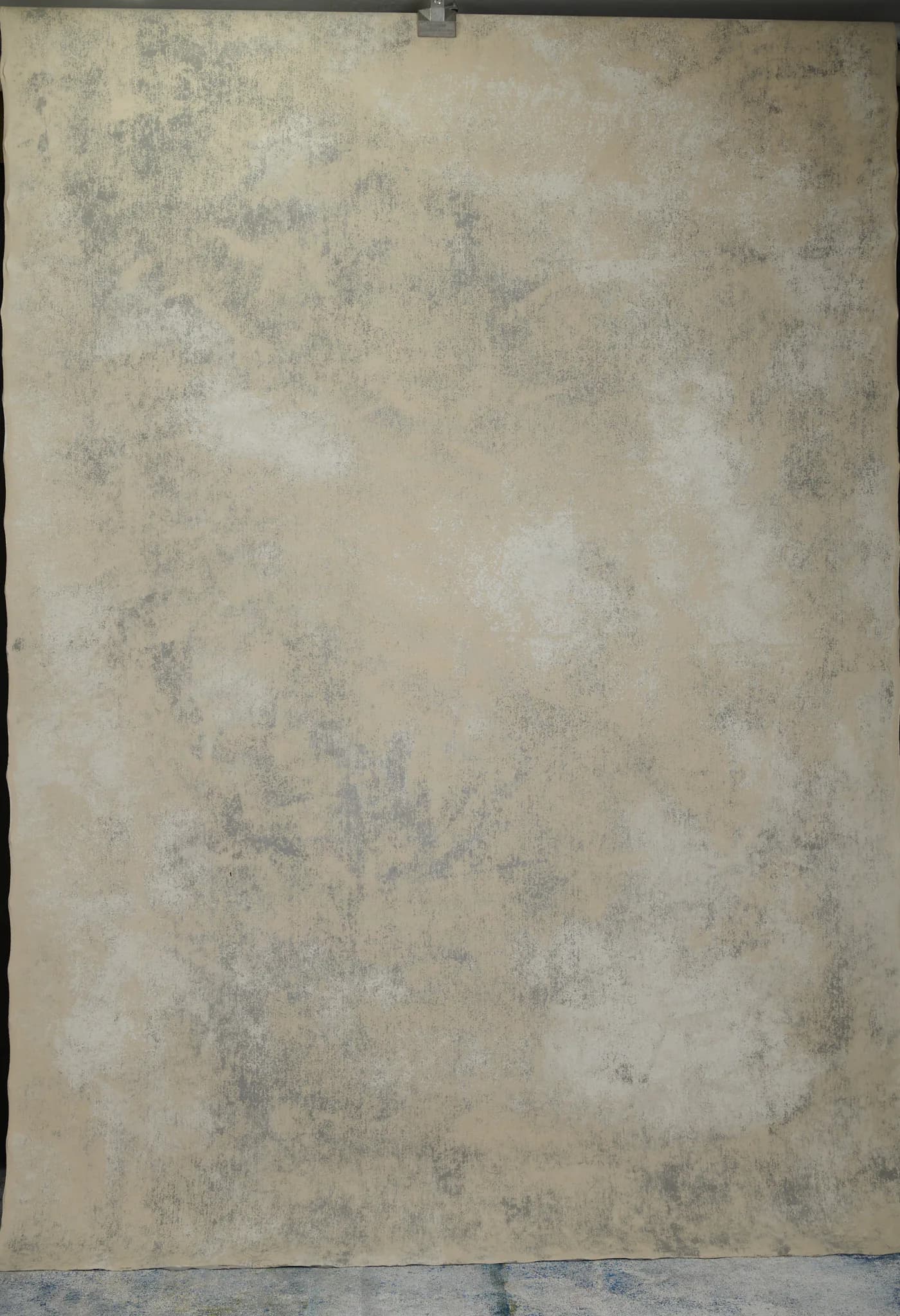 The back of a grey hand-painted canvas backdrop hanging full length: cream canvas with grey drifts and cloudy patches where the paint soaked through